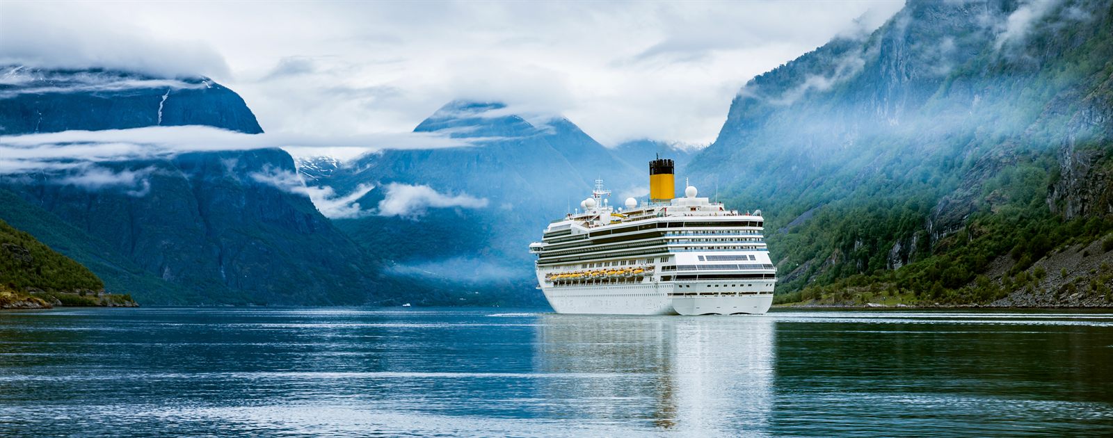 Cruise ship sailing through a calm Norwegian fjord between steep green mountains
