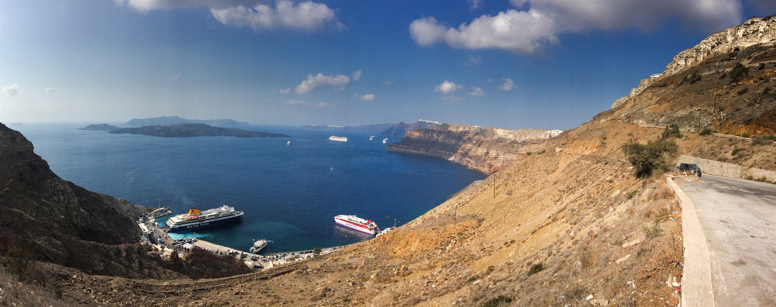 Cruise ships at anchor in the blue caldera below a dry Greek island hillside
