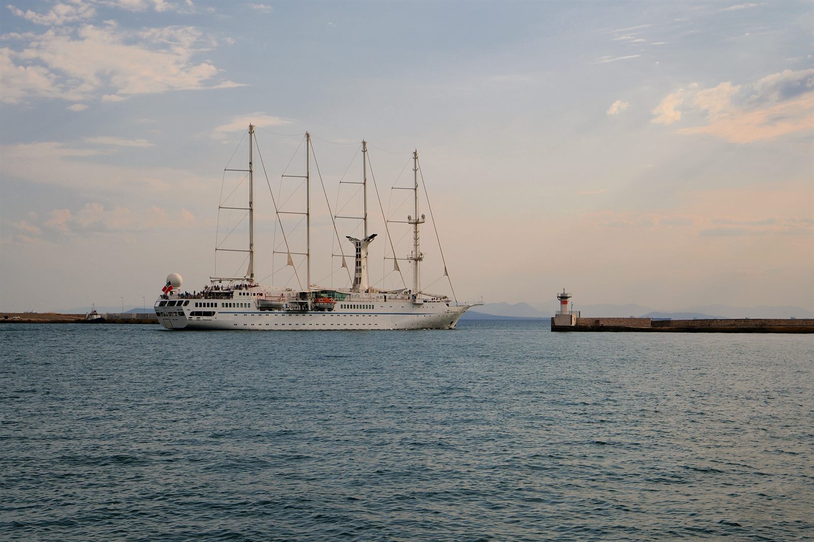 Two tall-masted sailing cruise ships at anchor near a harbor breakwater