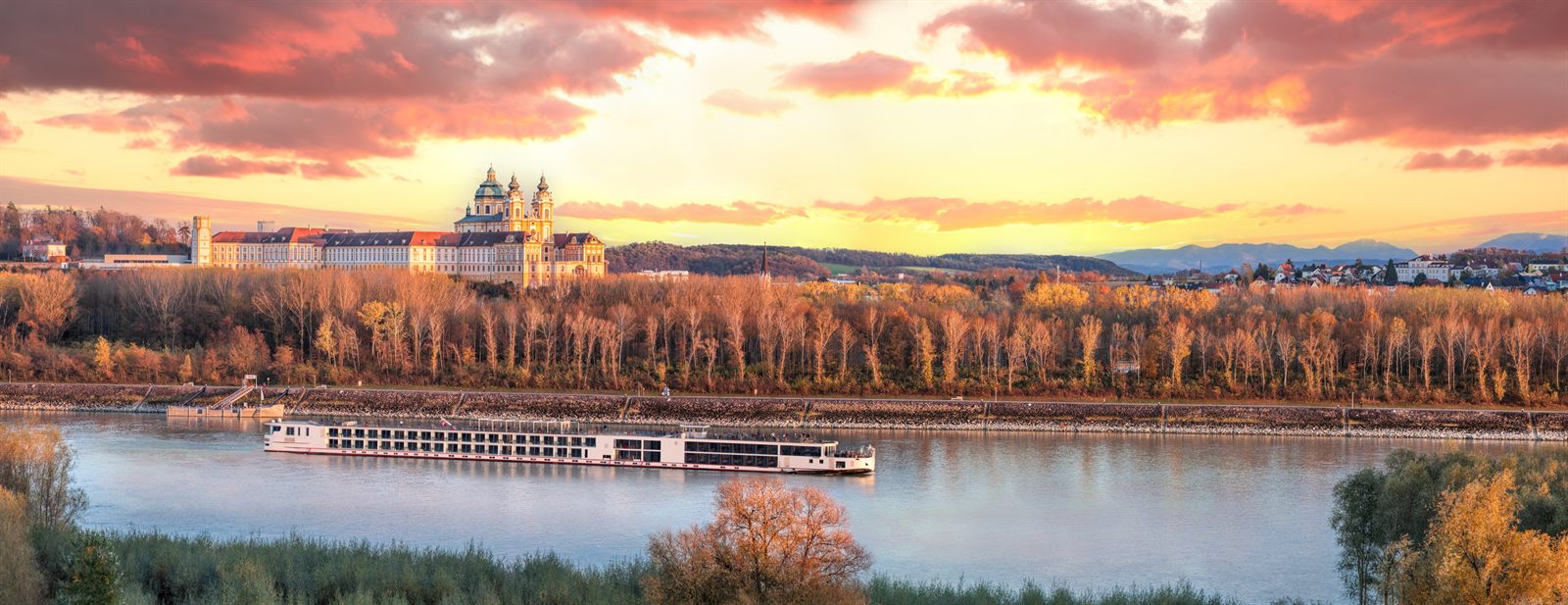 River cruise ship on the Danube below a hilltop abbey at sunset